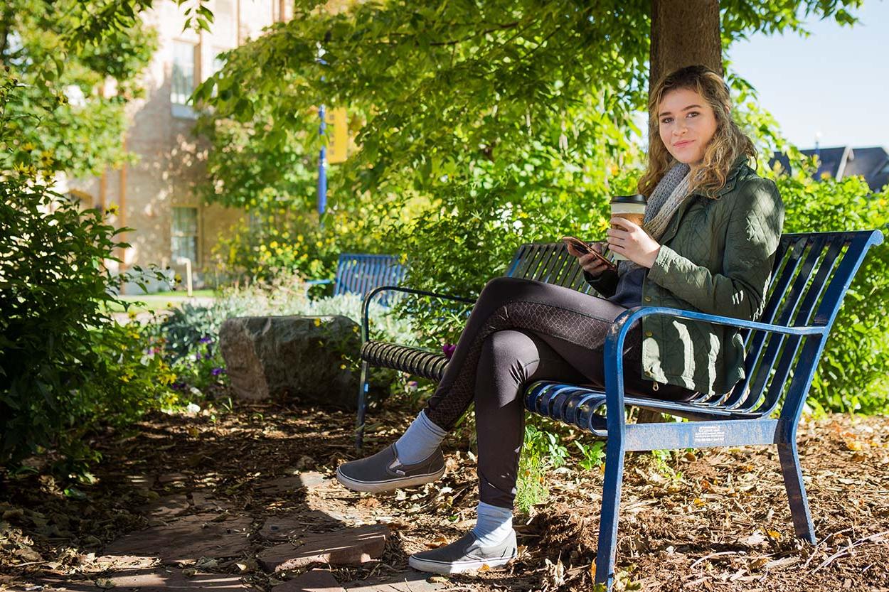 Student sits on a bench drinking coffee.